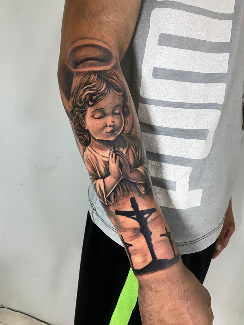 Tatuagem de anjo em oração e cruzes no antebraço