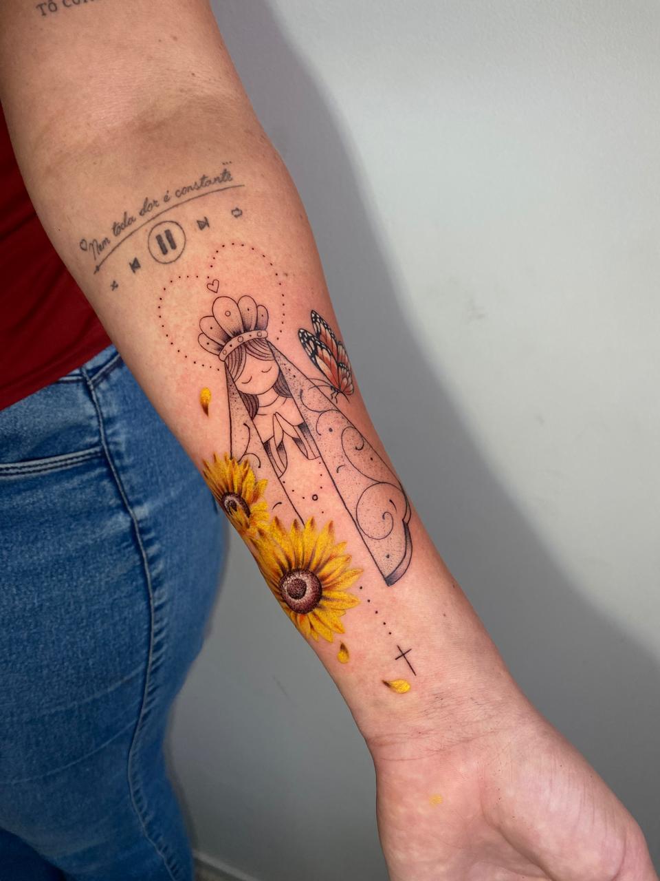 Tatuagem fineline de Nossa Senhora com girassóis coloridos no antebraço