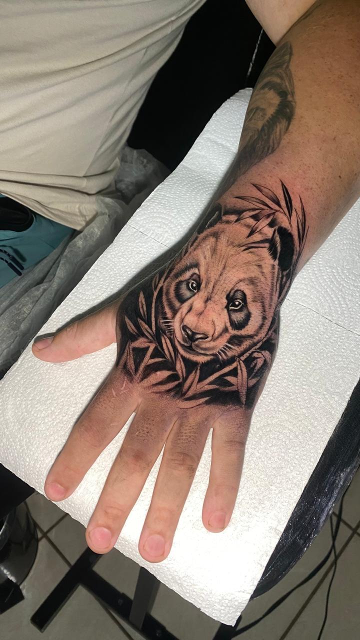 Tatuagem de panda entre bambus na mão, realismo preto e cinza